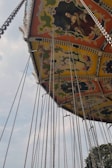 An ornate amusement park swing ride is depicted with colorful patterns and chains hanging down. The ride features painted panels with classical artwork. The sky is partially cloudy, adding to the vintage feel of the scene.