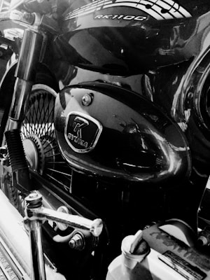 A close-up view of a motorcycle engine with visible branding and design elements. Notable features include metallic components and spoked wheels, emphasizing the mechanical aspects. The image is in black and white, highlighting reflections and textures.
