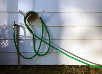 Close-up of a retractable garden hose reel mounted neatly on a garden wall surrounded by blooming flowers.