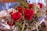 A bouquet of vibrant red roses and green leaves intermixed with small white flowers. The roses are central and prominent, with their petals beautifully unfurled. The green leaves and stems add a fresh contrast to the bright red roses, while white flowers provide delicate accents.