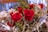 A bouquet of vibrant red roses and green leaves intermixed with small white flowers. The roses are central and prominent, with their petals beautifully unfurled. The green leaves and stems add a fresh contrast to the bright red roses, while white flowers provide delicate accents.