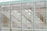 The image features a modern architectural facade composed of large glass panels. Through the glass, reflections of stone walls and window structures can be seen, creating a layered and abstract visual effect.