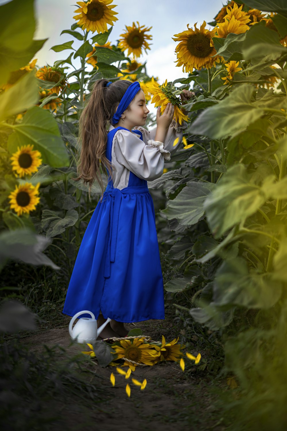 a little girl in a blue dress standing in a field of sunflowers