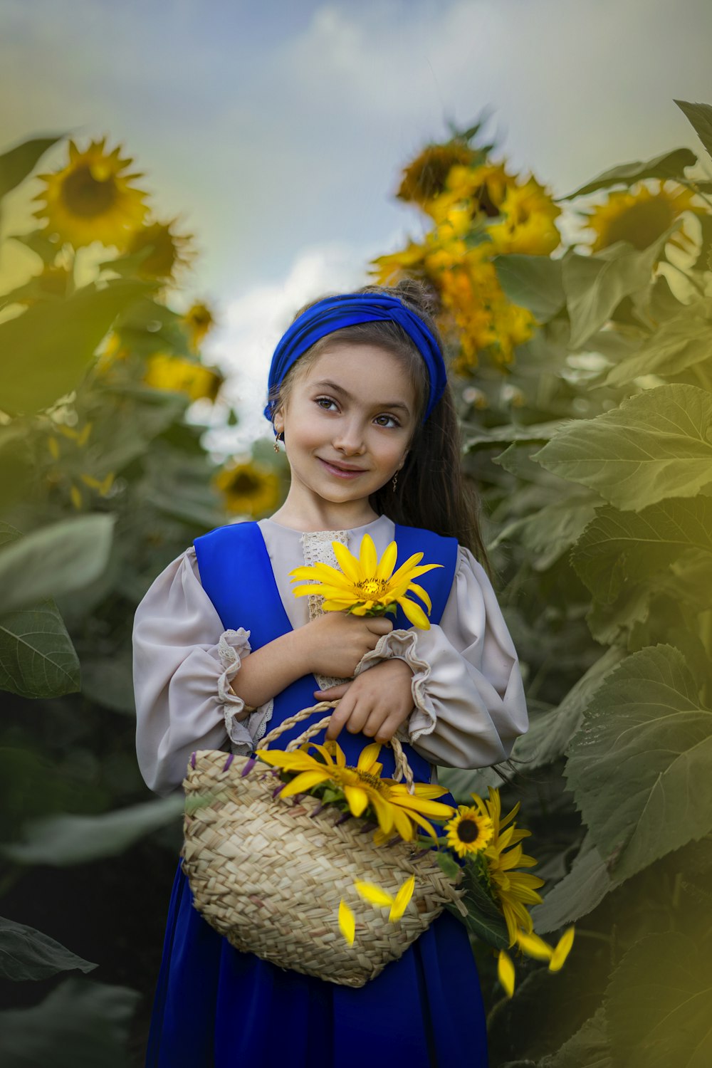 a young girl in a blue dress holding a basket of sunflowers
