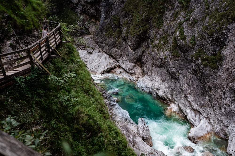 a wooden bridge over a river next to a cliff