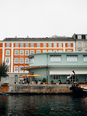 Cozy hotel facade overlooking the waterfront with people enjoying outdoor seating.