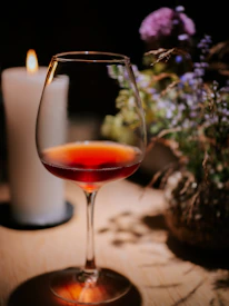 A glass of deep red wine catching warm light beside a charcoal gray tablecloth.