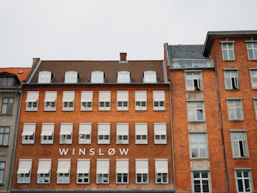 A row of multi-story brick buildings is depicted with a variety of windows. One of the buildings has the word 'WINSLOW' prominently displayed on its facade, which is characterized by symmetrical rows of windows with white frames.