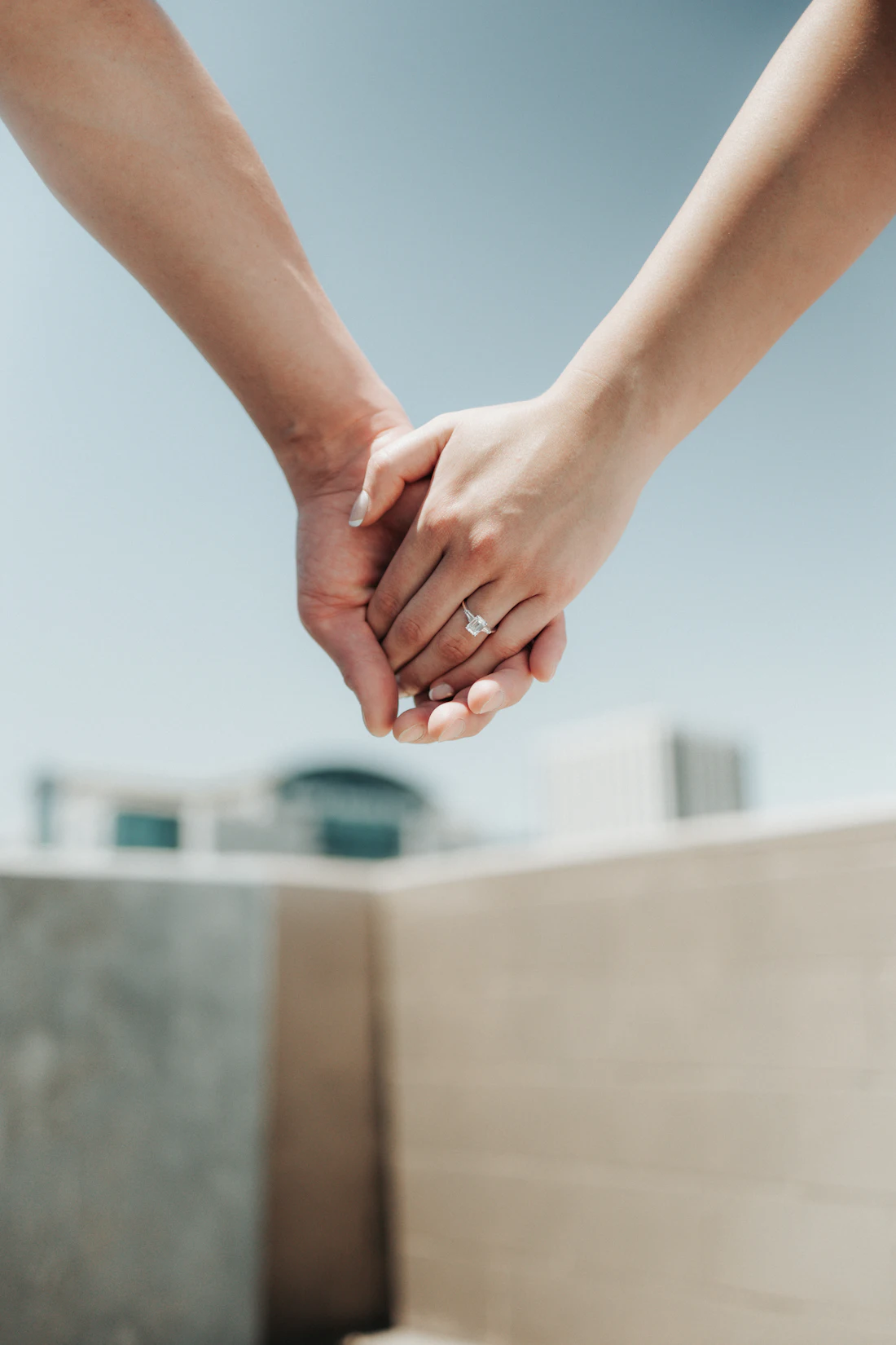 Close-up of two people holding hands, an engagement ring visible.