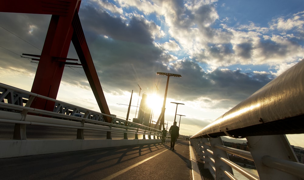the sun is setting over a bridge with a person walking on it
