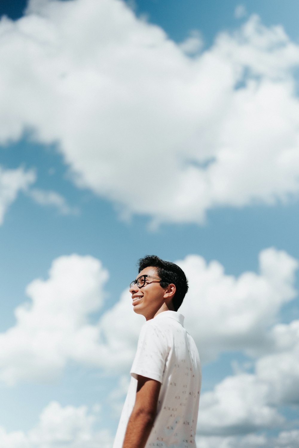 a man in a white shirt and glasses standing under a cloudy blue sky