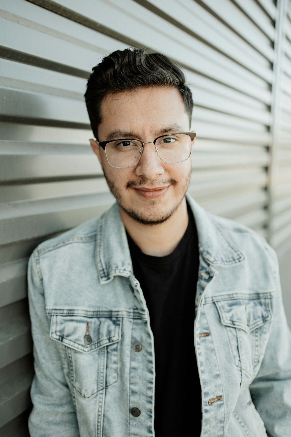 a man wearing glasses leaning against a wall