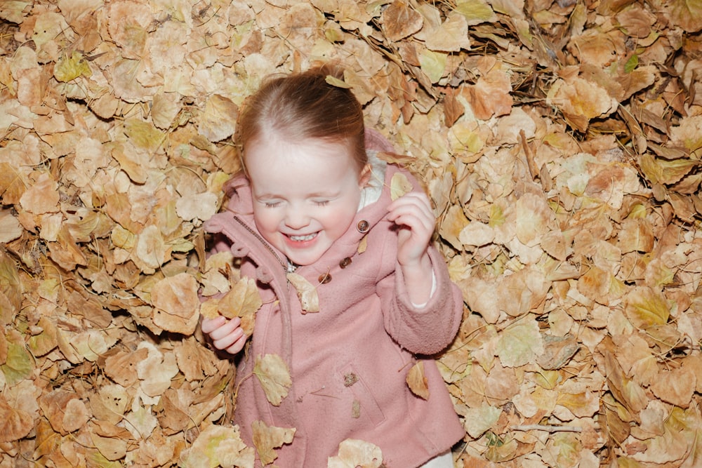 a little girl laying on a pile of leaves talking on a cell phone