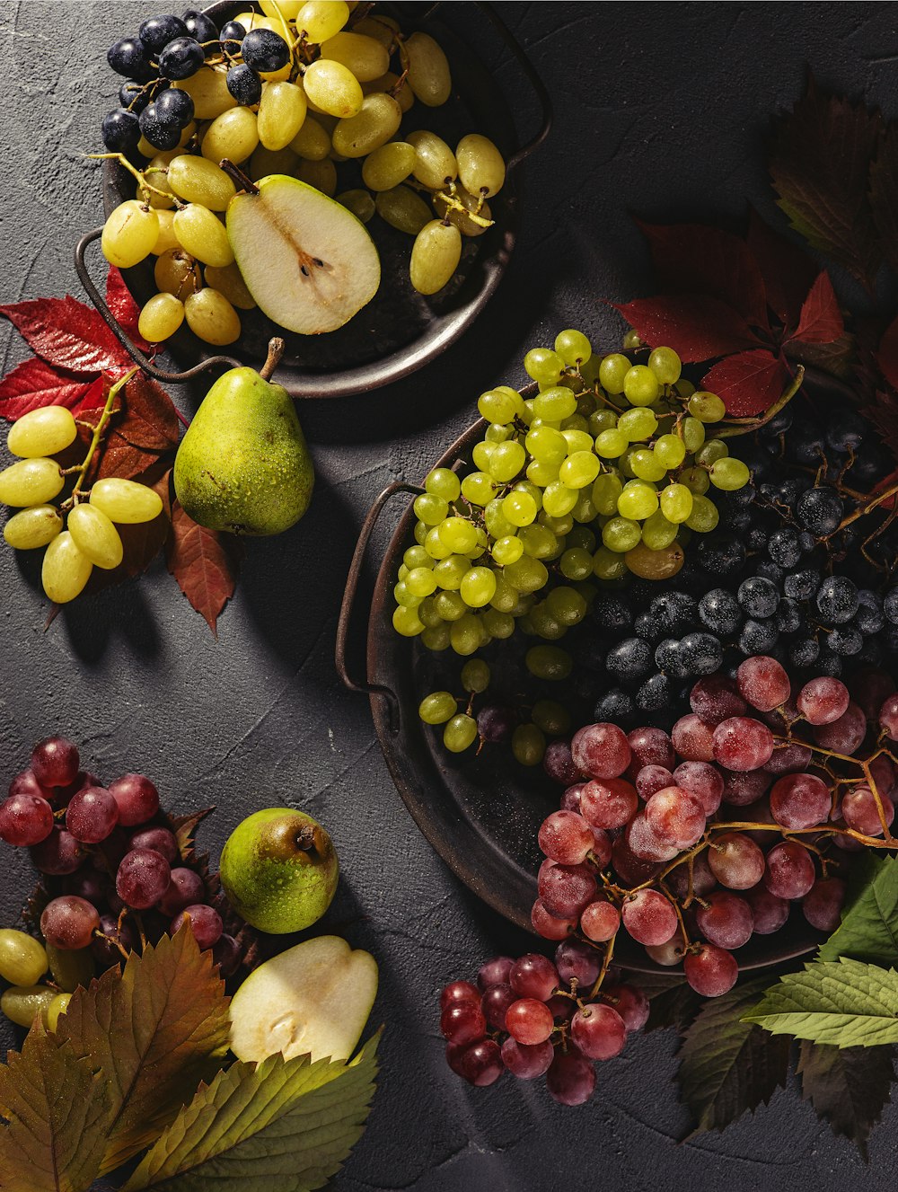 a plate of grapes, pears, apples, and leaves