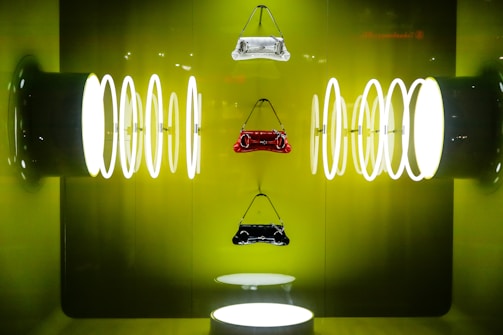 Three handbags are suspended against a vibrant green backdrop, surrounded by a series of illuminated circular rings on both sides, creating a symmetrical and futuristic display.