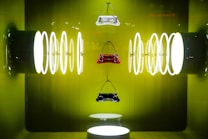 Three handbags are suspended against a vibrant green backdrop, surrounded by a series of illuminated circular rings on both sides, creating a symmetrical and futuristic display.