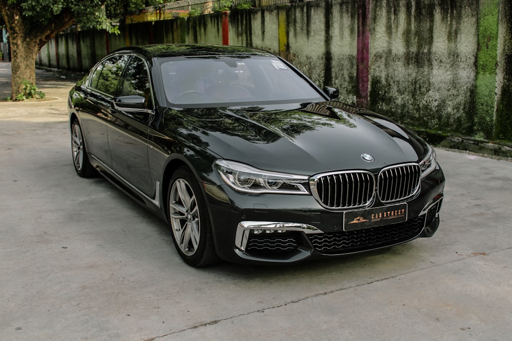 a black car parked in a driveway next to a tree