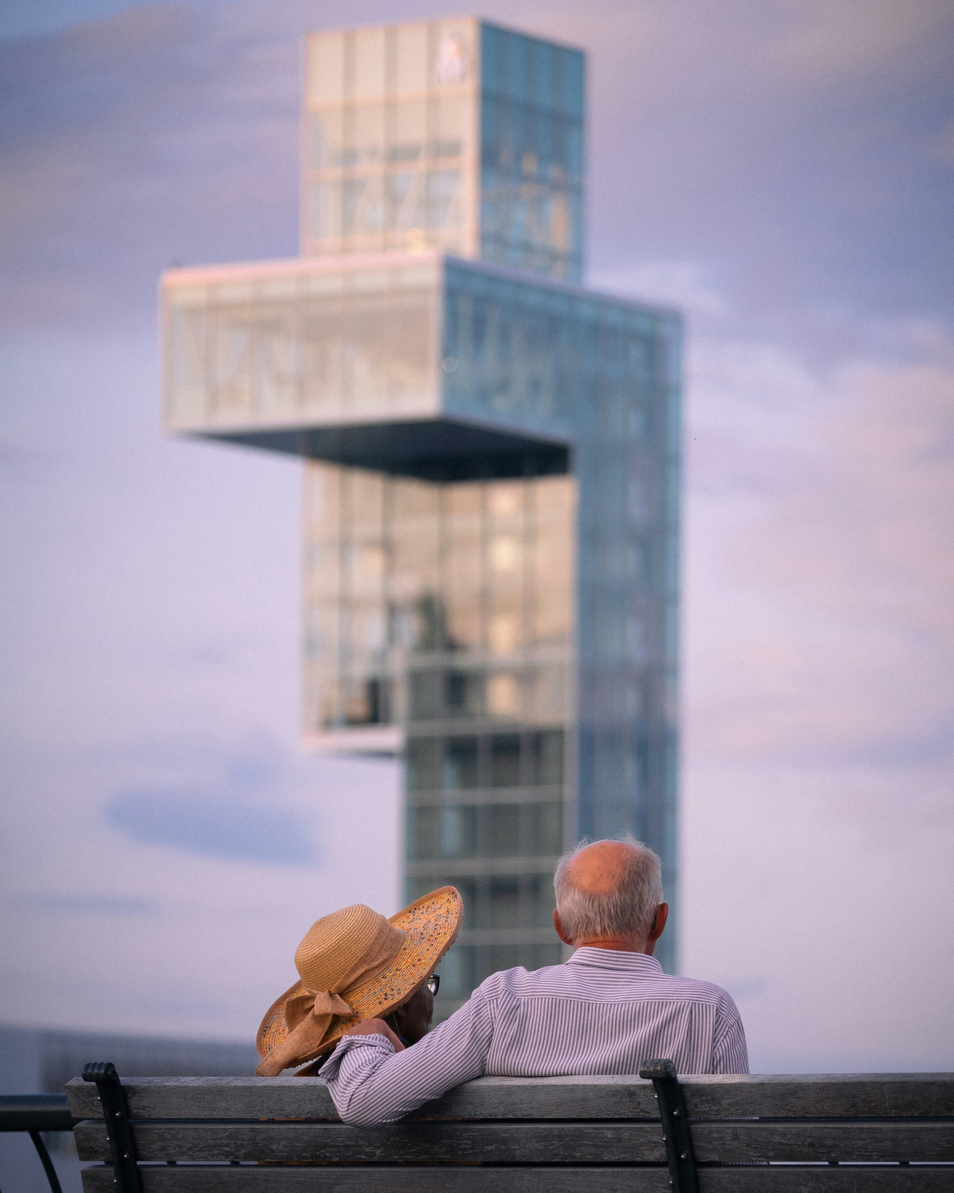 two people sitting on a bench looking at a tall building