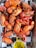 A platter filled with seasoned and cooked crawfish, displaying a vibrant red-orange color. The crawfish are presented on a checkered black and white paper, accompanied by a small clear dish containing melted butter or oil.