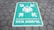 A painted sign on a hexagonal tile floor shows a green rectangle with white symbols. It contains human figures and arrows pointing inward, accompanied by the text 'TITIK KUMPUL'.