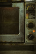 An old, well-used oven with dials and settings for different cooking temperatures and modes. The oven's metal exterior appears worn and dirty, likely from frequent use over time. There is a small red light indicating that part of the appliance is on.