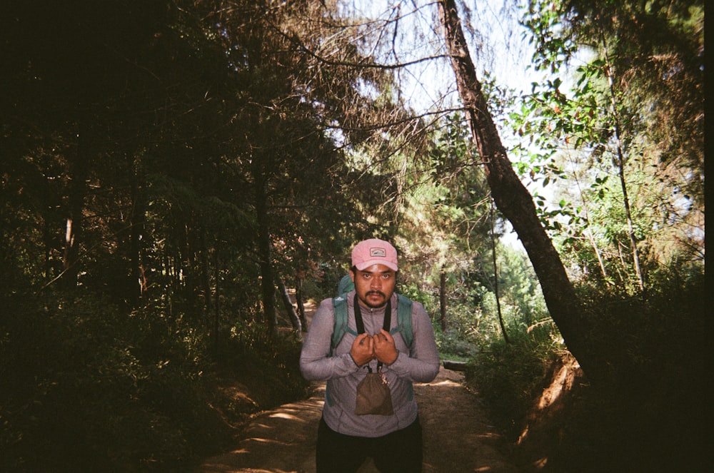 a man with a pink hat and backpack standing in the woods