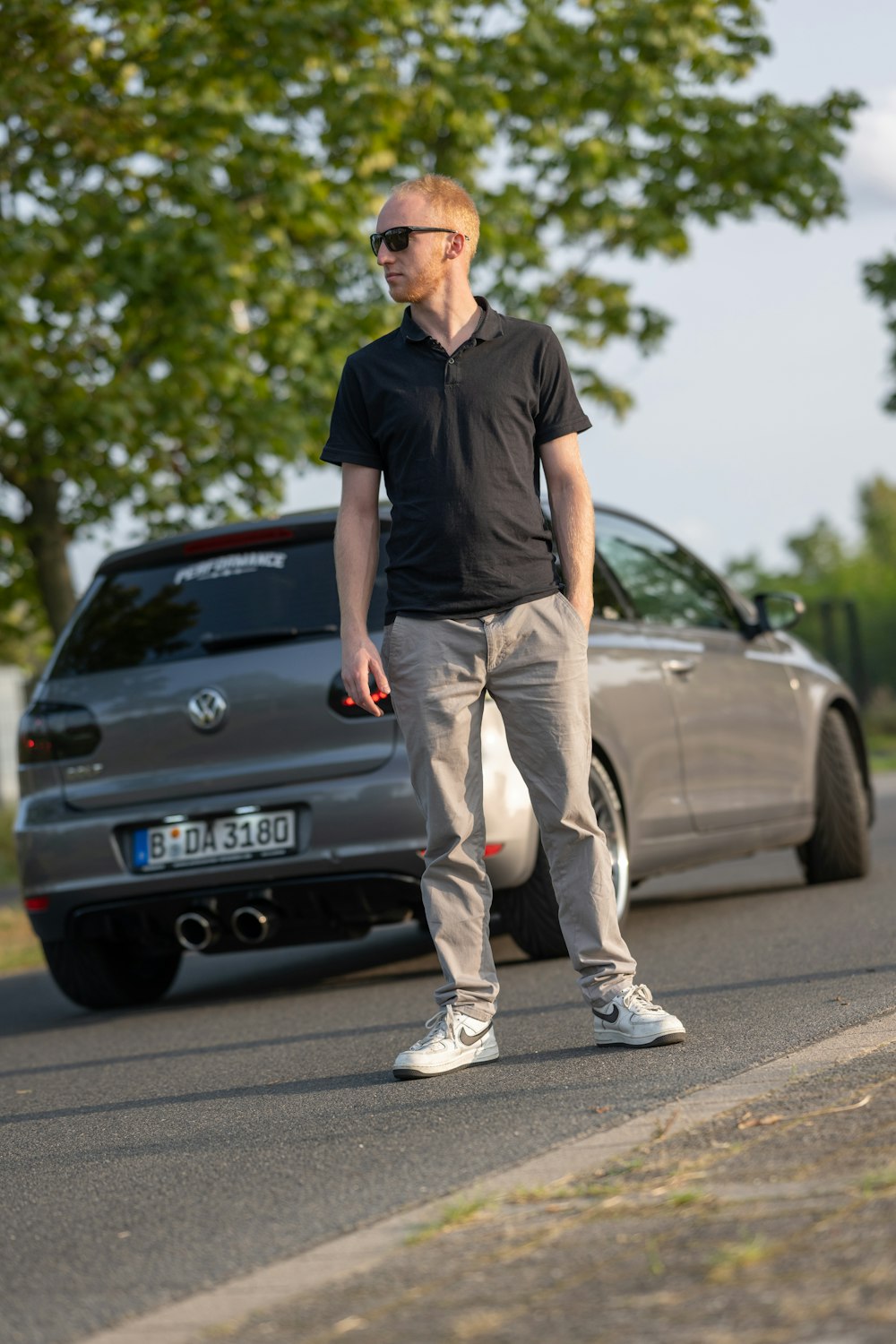 車の隣の道路脇に立っている男