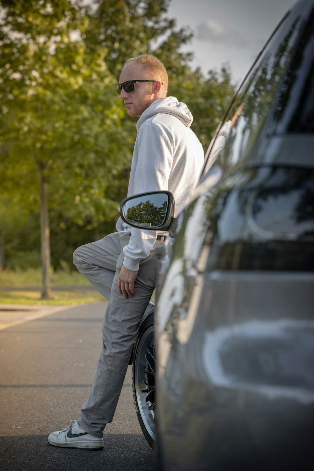 a man in a white hoodie leaning against a car