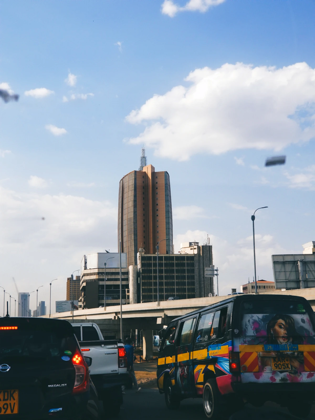 A group of cars driving down a street next to tall buildings