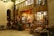 A cozy, warmly lit shop with a rustic wooden exterior, showcasing a variety of traditional handicrafts and decorative items. Colorful textiles, baskets, and dolls are displayed outside, inviting visitors to explore inside where more goods are visible through the glass windows. The scene is serene with a hint of nostalgia.