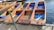 Wooden boats with blue cushions are aligned on a dock, chained and ready for use on the water. Each boat has a unique identification number and a paddle rests across one of them.