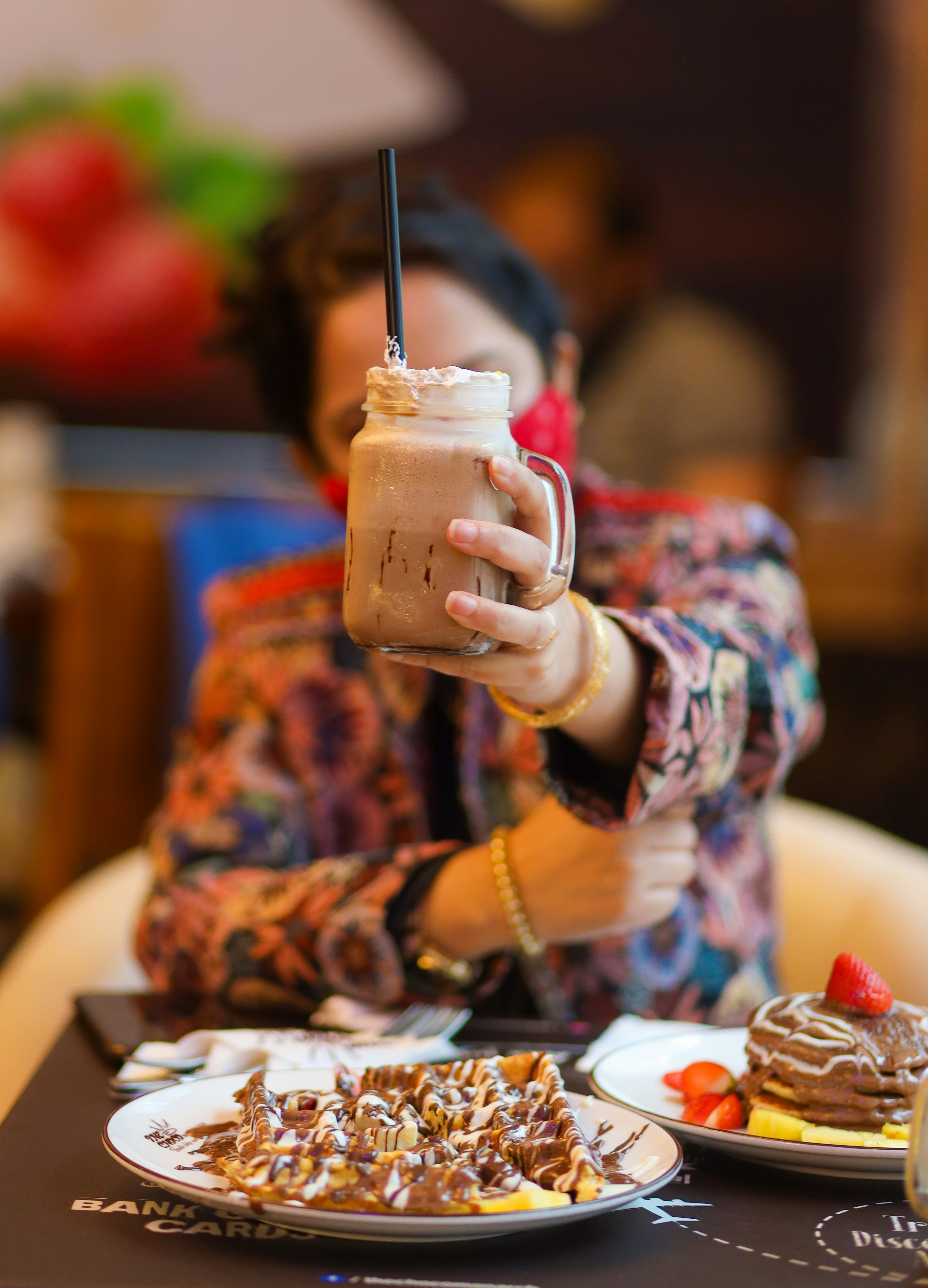 a woman holding a drink over a plate of food