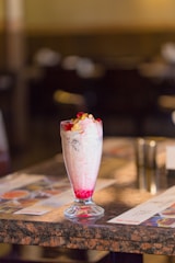 A vibrant close-up of a creamy, colorful shake topped with fresh fruit and a sprinkle of nuts, set against a rustic wooden table.