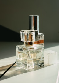 Several perfume bottles are arranged on a flat surface, reflecting light and casting soft shadows. The setup appears elegant, with a transparent design that showcases the liquid inside. The background is minimal, emphasizing the products.