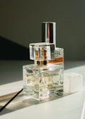 Several perfume bottles are arranged on a flat surface, reflecting light and casting soft shadows. The setup appears elegant, with a transparent design that showcases the liquid inside. The background is minimal, emphasizing the products.
