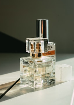Several perfume bottles are arranged on a flat surface, reflecting light and casting soft shadows. The setup appears elegant, with a transparent design that showcases the liquid inside. The background is minimal, emphasizing the products.