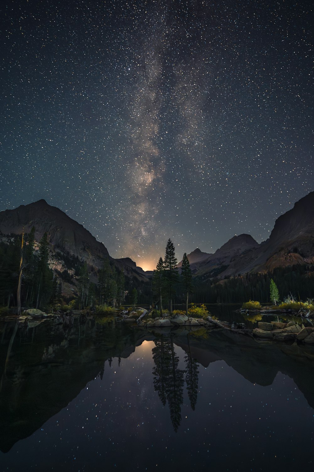 Il cielo notturno si riflette nell'acqua ferma di un lago di montagna