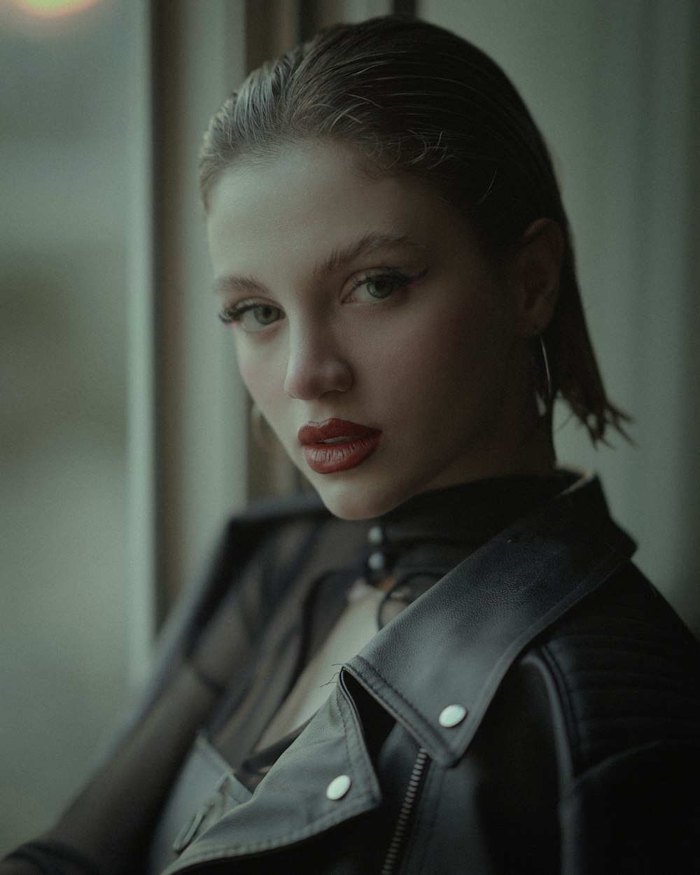 a woman in a leather jacket looking out a window