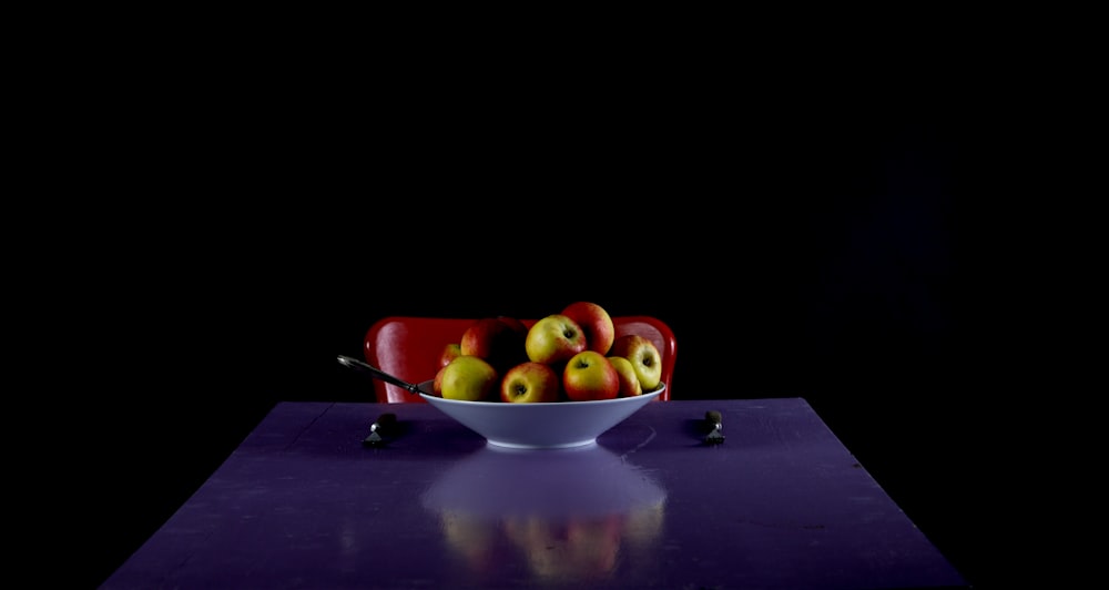 a bowl filled with apples sitting on top of a table