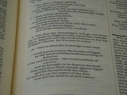 A close-up view of an open book page from the Bible, showing printed text in English. The text is clearly legible and features biblical verses with some words in bold and small numbers indicating verse numbers.