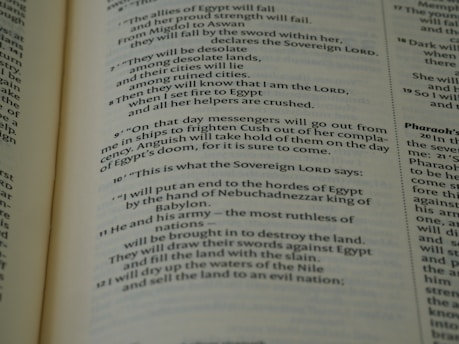 A close-up view of an open book page from the Bible, showing printed text in English. The text is clearly legible and features biblical verses with some words in bold and small numbers indicating verse numbers.