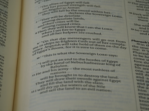 A close-up view of an open book page from the Bible, showing printed text in English. The text is clearly legible and features biblical verses with some words in bold and small numbers indicating verse numbers.