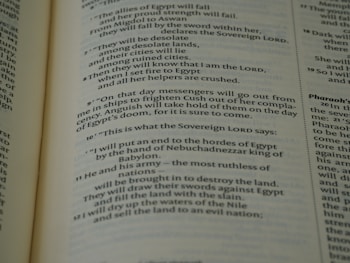 A close-up view of an open book page from the Bible, showing printed text in English. The text is clearly legible and features biblical verses with some words in bold and small numbers indicating verse numbers.