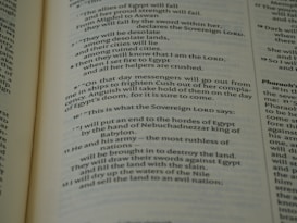 A close-up view of an open book page from the Bible, showing printed text in English. The text is clearly legible and features biblical verses with some words in bold and small numbers indicating verse numbers.