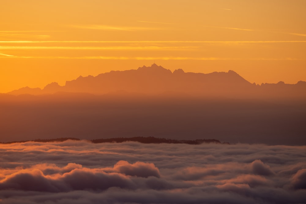 the sun is setting over the mountains above the clouds