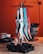 A collection of colorful hookah tongs, including black, white, teal, and red, hanging on a hookah setup. Below them, black charcoal cubes are arranged on a wooden surface. The background features an orange backdrop and a metallic container.