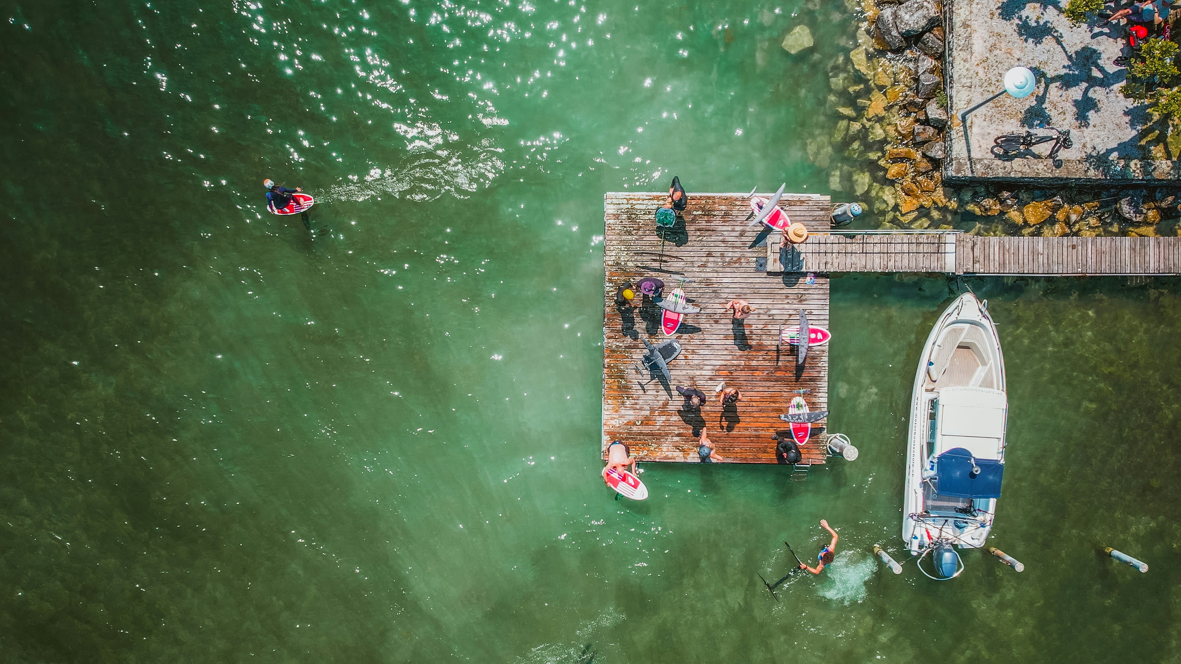 Des gens font de la planche à pagaie et nagent près d'un bateau à un quai en bois.