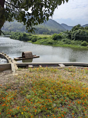 A serene river view with a rustic boat framed by lush greenery and rocky hills.