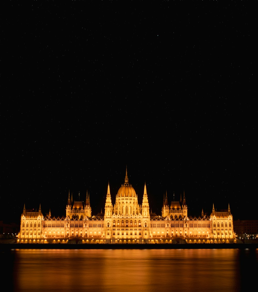 Un grand bâtiment éclairé la nuit avec de l’eau devant lui