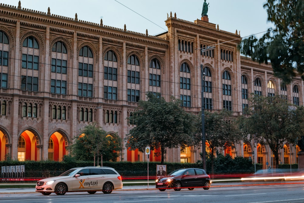 two cars driving down a street in front of a large building